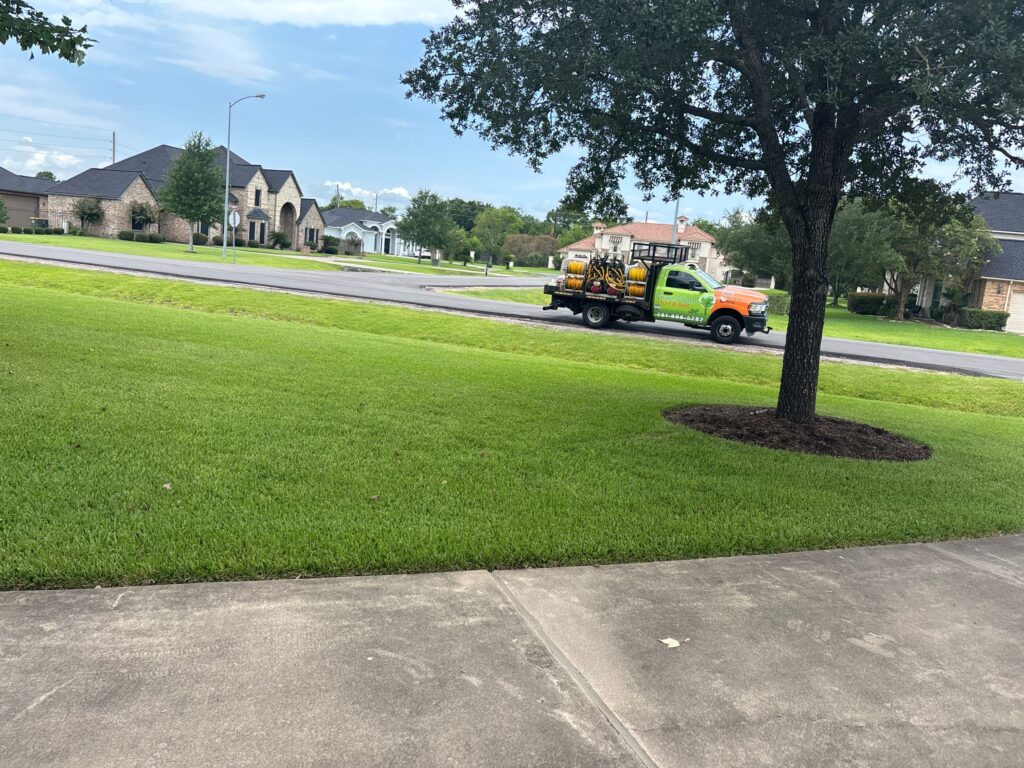 Zoomed out photo of a green lawn and greengate truck near the road that provided a lawn aeration service