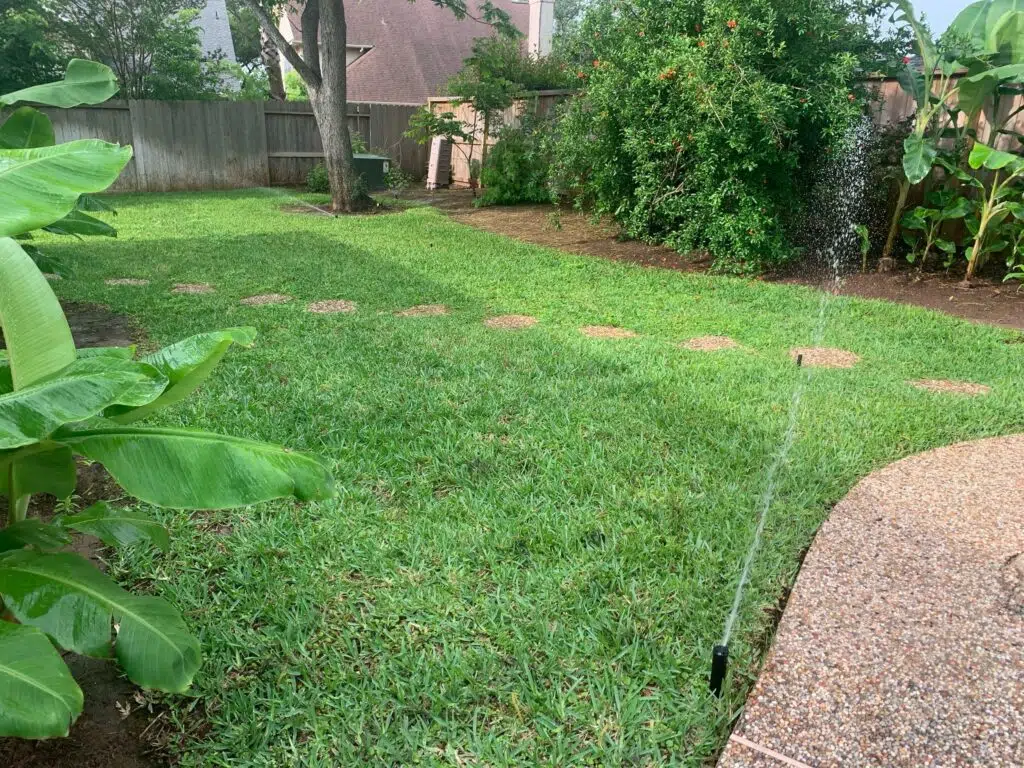Sprinklers running in a backyard while a sprinkler repair company is doing repairs