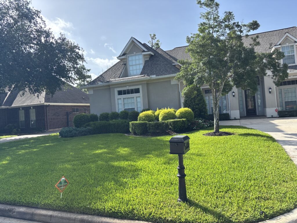 View from the street of a green lawn with a greengate sign in the grass after a lawn fertilizer service