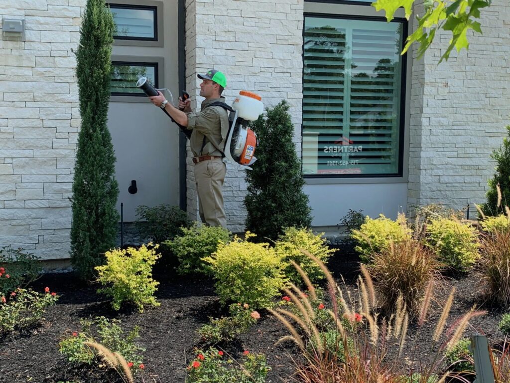 GreenGate technician spraying a mosquito barrier near a house along with in2care mosquito traps