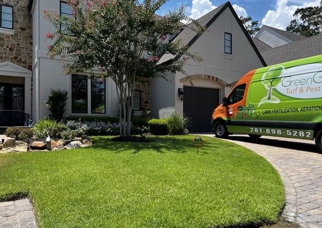 View of a home and green front yard with a greengate van parked in the driveway during ant control services and chinch bug treatment