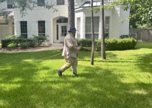 Technician applying pre emergent vs post emergent on a green lawn in front of a white house