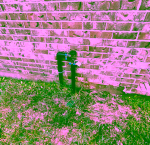 Photo of a backflow preventer leaking, causing mud around the backflow preventer unit on side of brick home