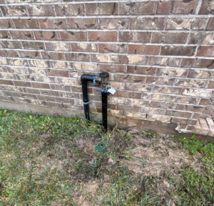 Photo of a backflow preventer leaking, causing mud around the backflow preventer unit on side of brick home
