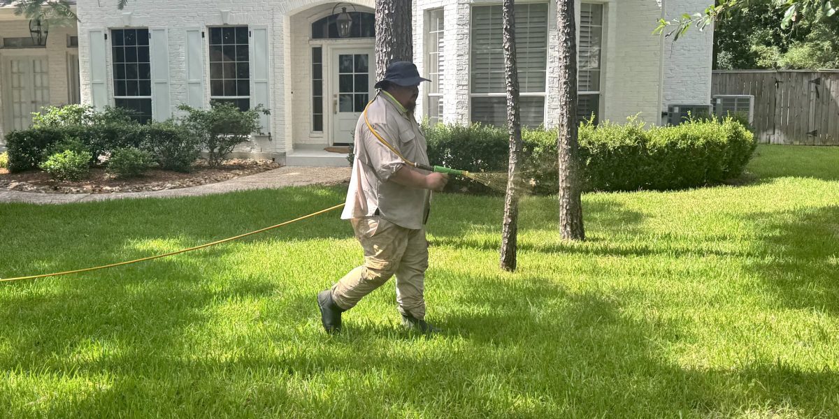 Technician applying pre emergent vs post emergent on a green lawn in front of a white house